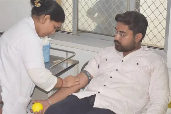 अस्पताल के वार्ड में कुर्सी पर बैठे युवक की बांह पर रक्तदान की प्रक्रिया करती स्वास्थ्यकर्मी