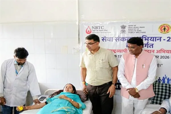अस्पताल के कक्ष में बिस्तर पर रक्तदान करती महिला, पास में स्वास्थ्यकर्मी और तीन अन्य लोग खड़े हैं