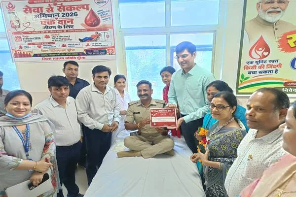 अस्पताल के कमरे में बिस्तर पर बैठे व्यक्ति को प्रमाणपत्र देते अधिकारी और आसपास खड़े स्वास्थ्यकर्मी व अन्य लोग