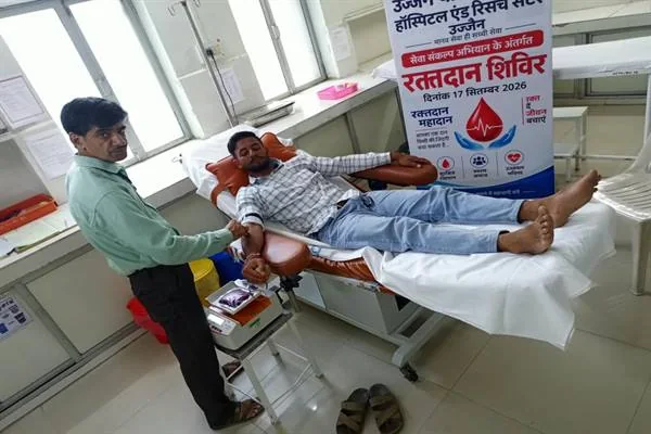 अस्पताल के कमरे में बेड पर लेटा एक व्यक्ति रक्तदान कर रहा है और पास में स्वास्थ्यकर्मी खड़ा है।