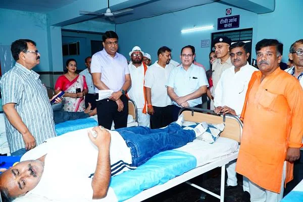 अस्पताल के बिस्तर पर लेटे रक्तदाता के आसपास खड़े अधिकारी, कर्मचारी और अन्य लोग