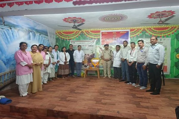 सजे हुए सभागार में दीप और आयुर्वेद दिवस के पोस्टर के पास खड़े स्वास्थ्यकर्मी, जेल अधिकारी और अन्य लोग